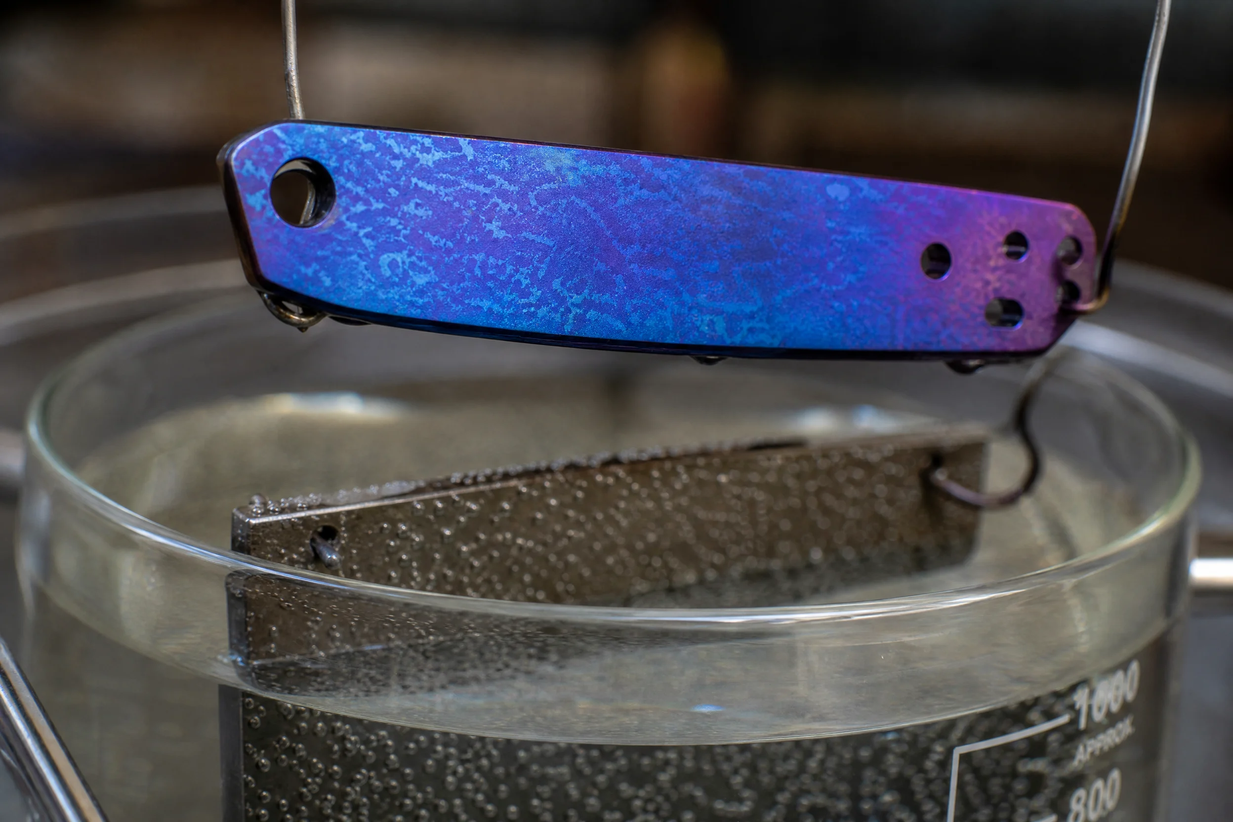 So eloxieren Sie Titan zu Hause: Die vollständige DIY-Anleitung (Spannungstabelle, Einrichtung der Stromversorgung und echte Ergebnisse) 5 Ein Titanstück, das während des Anodisierungsprozesses in einem Elektrolytbad eingetaucht ist und an dessen Metalloberfläche sich eine blau-violette Färbung bildet